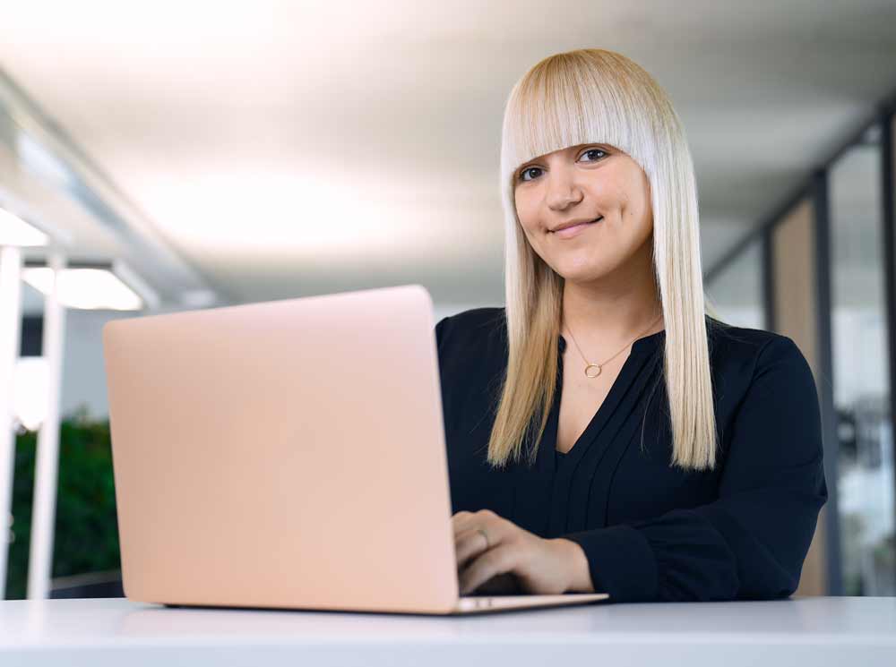 Junge, blonde Frau tippt auf Laptop beim Webinar" title="Luise-Bickel-V3