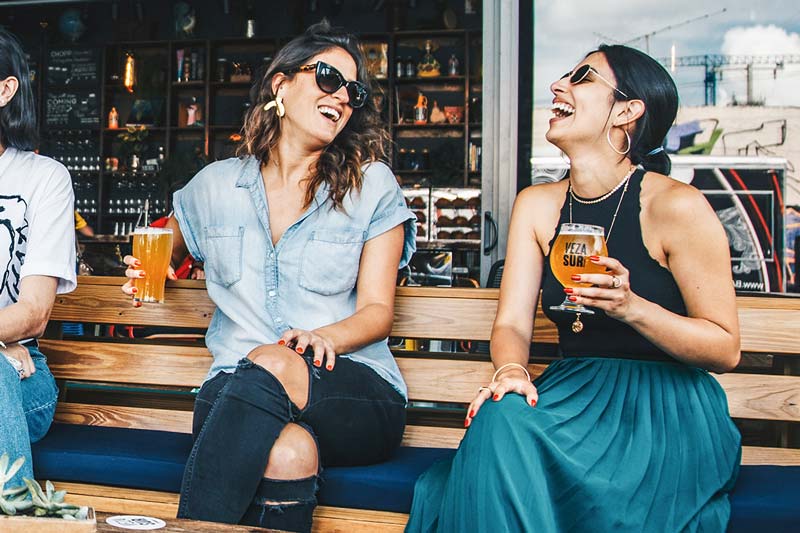 Zwei Frauen sitzen in einer Bar draußen und lachen zusammen: Soziale Nachhaltigkeit in Unternehmen" title="Blog-Nachhaltigkeit-Bild