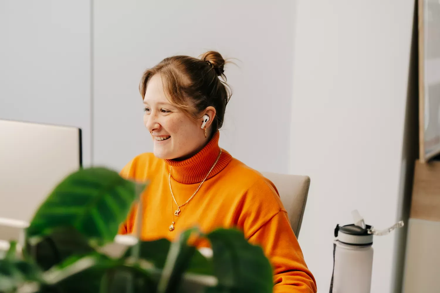 Frau mit orangenem Outfit sitzt lachend am Schreibtisch: intrinsische Motivation fördern