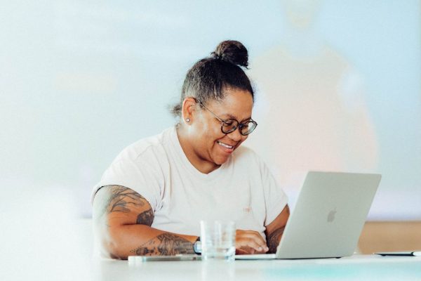 eine Frau sitzt an einem Schreibtisch mit Laptop" title="e2n academy mit Tina