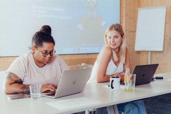 zwei Frauen sitzen an einem Schreibtisch mit Laptop" title="e2n academy mit Tina und Nina