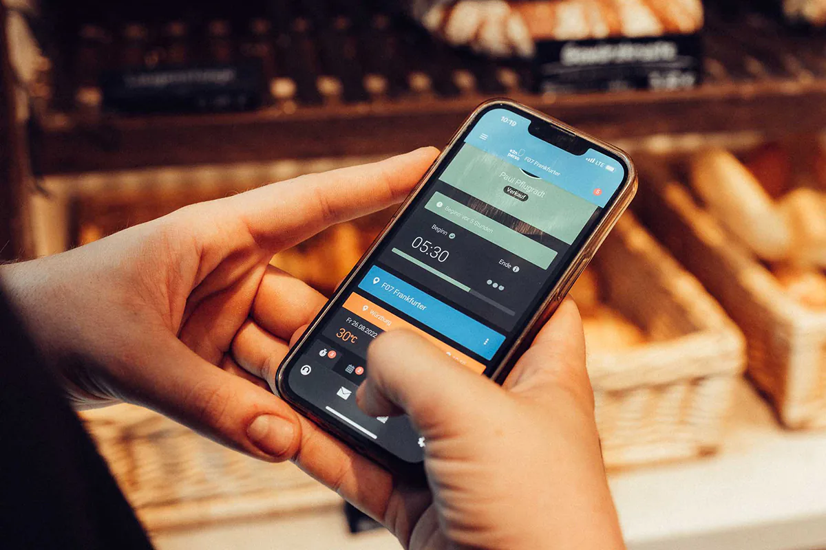 Eine Person hält ein Handy in der Hand und hat die e2n perso App geöffnet" title="Digitale Zeiterfassung mit e2n perso