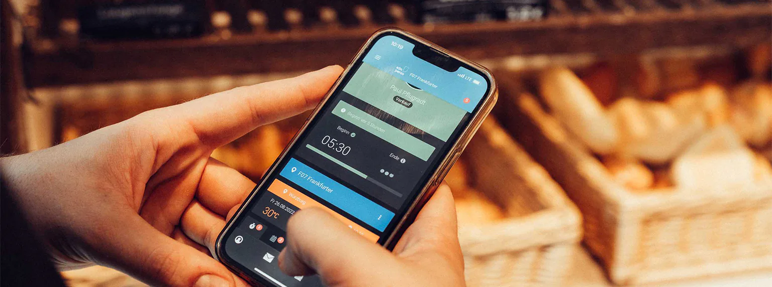 Eine Person hält ein Handy in der Hand und hat die e2n perso App geöffnet" title="Digitale Zeiterfassung mit e2n perso