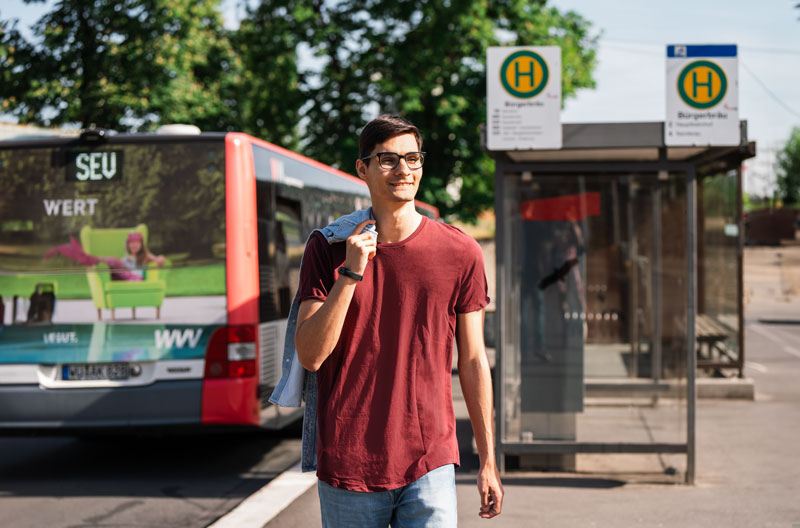 Mann im casual Businessoutfit steht vor einem Bus an der Bürgerbräu Haltestelle und steigt aus." title="mann-bahnsteig-business