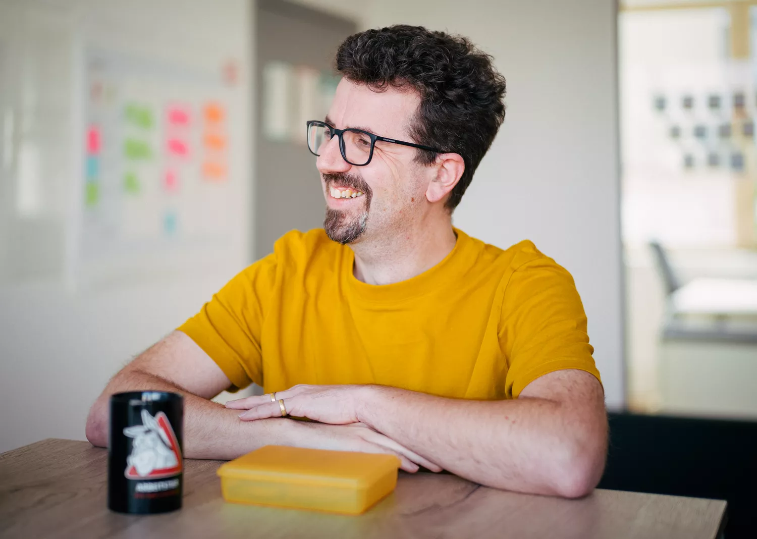 Junger Mann in orange-gelben Shirt & Brille lächelt an einem Tisch zur Seite" title="Urlaubsanspruch-Alexander-Dotor-Mohring-e2n-header