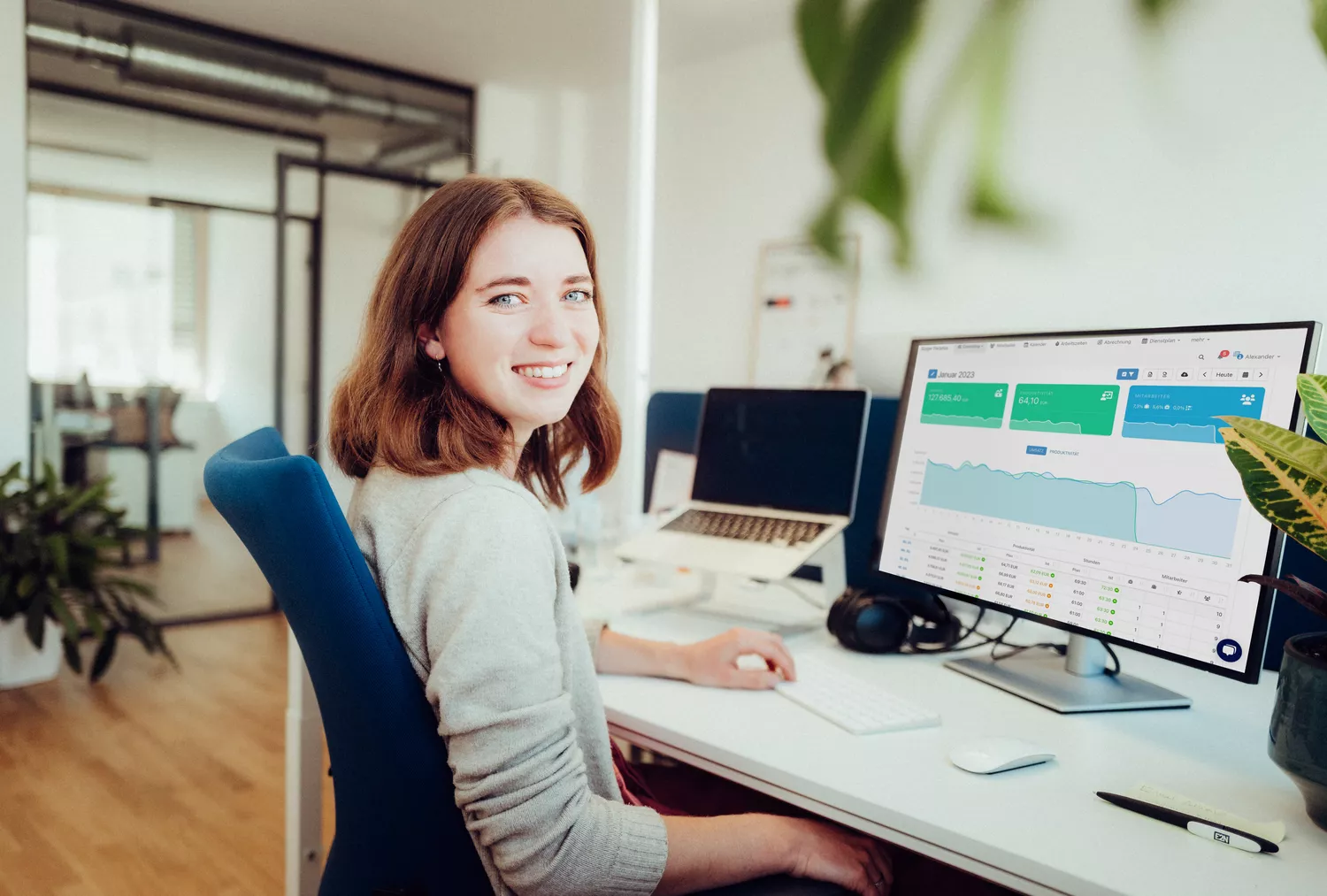 Sonja arbeitet am e2n manager in einem hellen und freundlichem Büro. Sie lächelt in die Kamera.