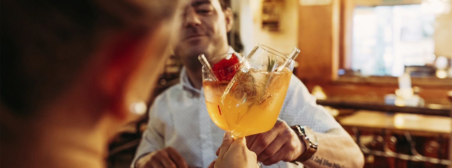 zwei Personen stoßen mit zwei Cocktails an auf die Senkung der Mehrwertsteuer in der Gastronomie