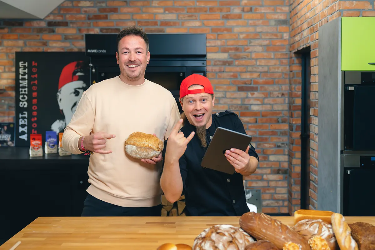 Philipp und Axel Schmitt lächeln mit Brot und Tablet in der Hand