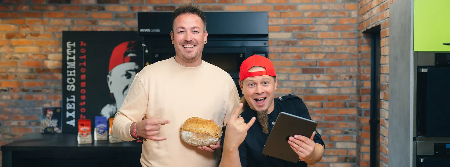 Philipp und Axel Schmitt lächeln mit Brot und Tablet in der Hand