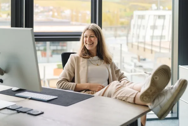 Corinna legt lächelnd die Füße auf dem Schreibtisch ab